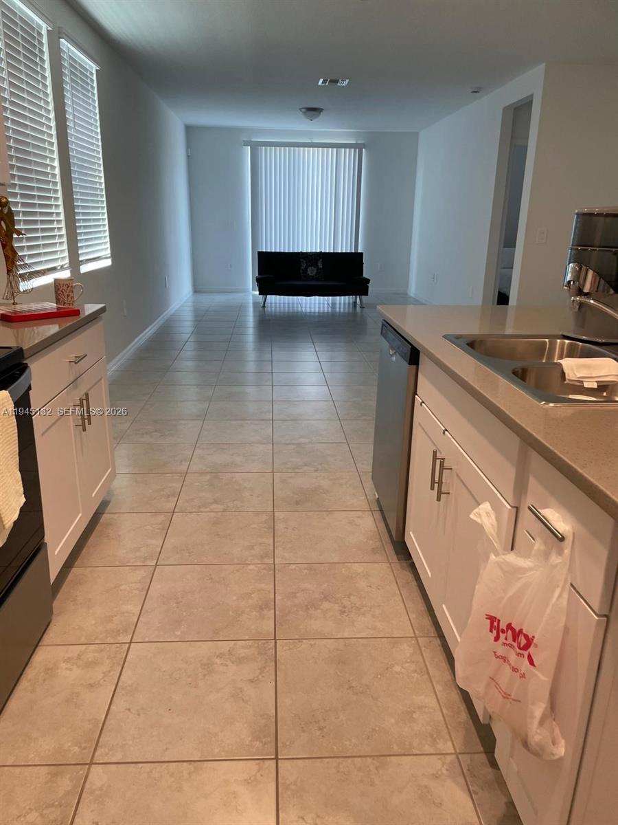 A kitchen with white cabinets and tile flooring opens into a living area with a sofa — 3829 GIORGIO, Winter Haven FL 33884, WINTER HAVEN, FL