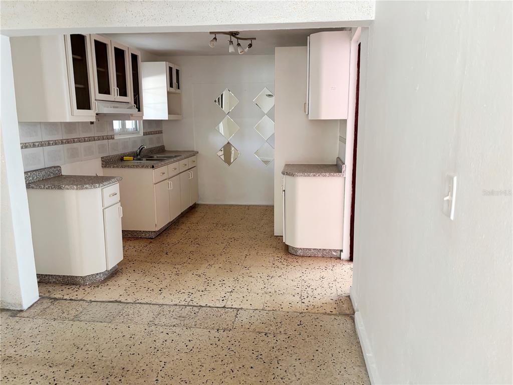 A kitchen with white cabinets, speckled flooring, and a ceiling fan in the adjacent area — Daniel Bonilla 30 BUENA VISTA, CAYEY, PR