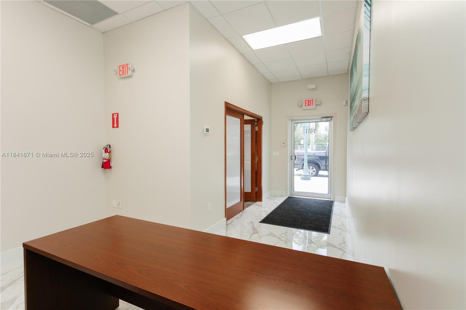 An office interior features a wooden desk, marble-look flooring, and a glass entrance door — 1911 Harrison St # 5, Hollywood FL 33020, HOLLYWOOD, FL