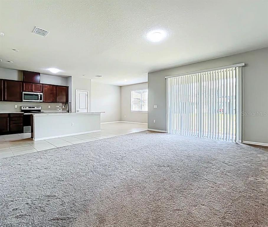 A spacious living room with gray carpet opens to a kitchen with dark wood cabinets — 2361 PALM PARK LOOP, CLERMONT, FL