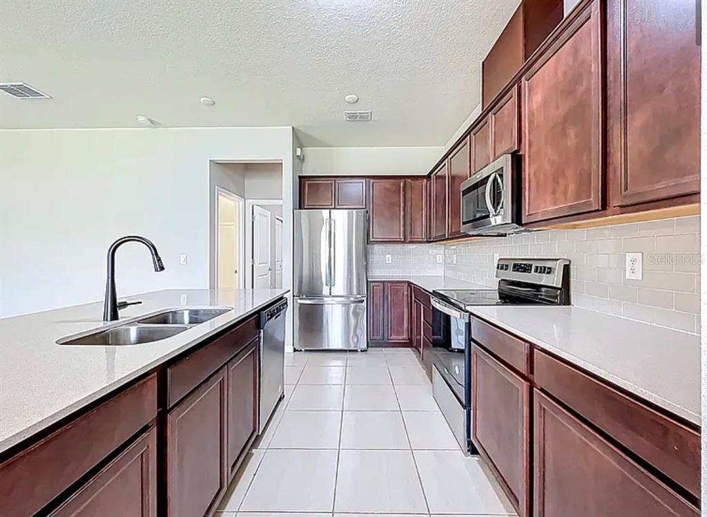 A kitchen with dark wood cabinets, stainless steel appliances, and a large quartz island — 2361 PALM PARK LOOP, CLERMONT, FL
