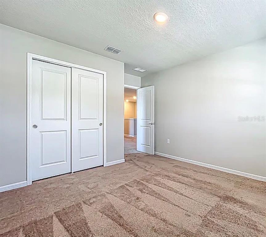 An empty bedroom features beige carpet, light gray walls, a white closet, and an open door — 2361 PALM PARK LOOP, CLERMONT, FL