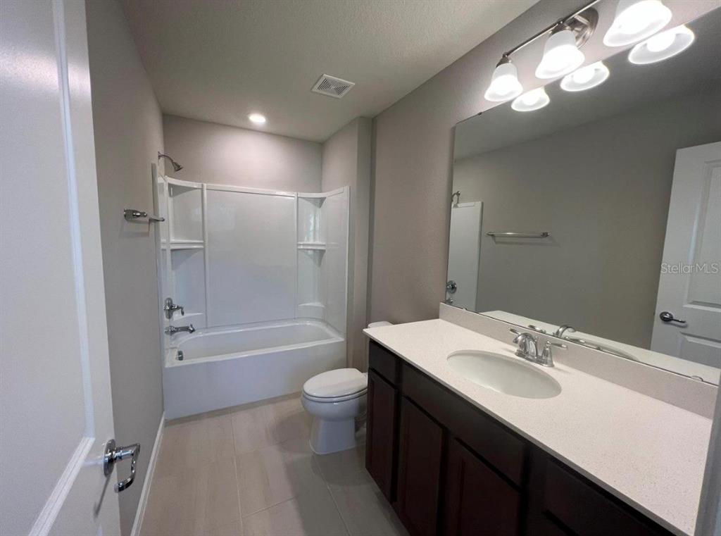 A bathroom features a white tub-shower combo, a dark wood vanity, and a large mirror — 2361 PALM PARK LOOP, CLERMONT, FL