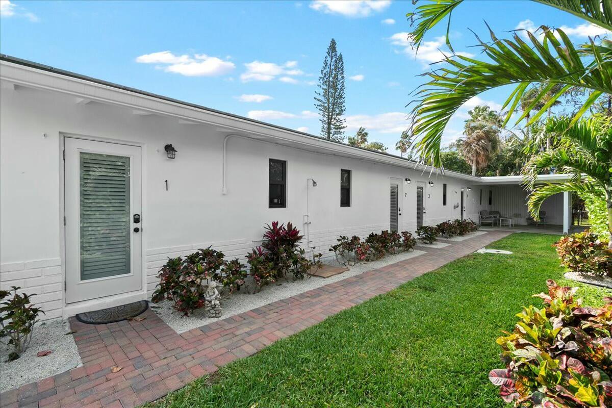 A white exterior building with numbered doors, a brick walkway, and tropical landscaping — 18 Adams Road, Ocean Ridge FL 33435, OCEAN RIDGE, FL