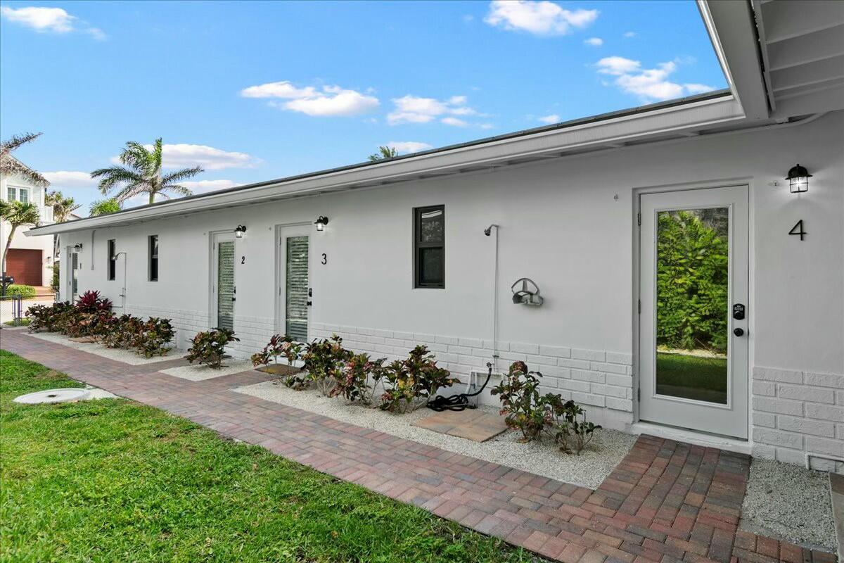A white exterior building features numbered doors, a brick walkway, and small landscaping beds — 18 Adams Road, Ocean Ridge FL 33435, OCEAN RIDGE, FL