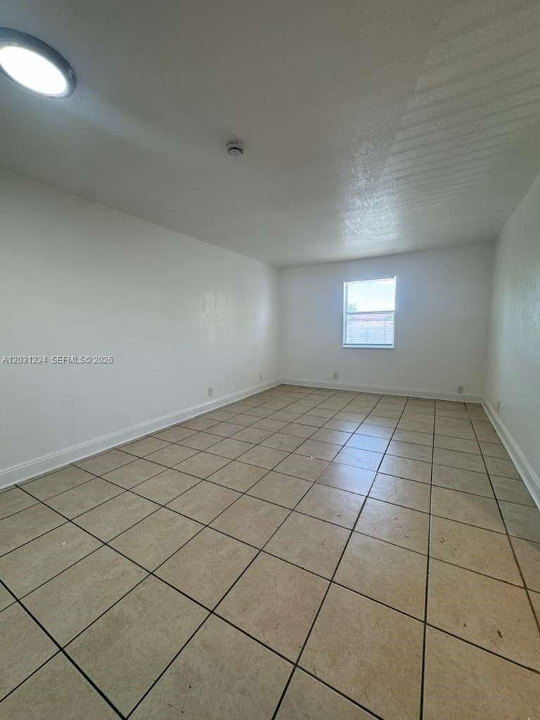 An empty room features white walls, a single window, and light-colored tiled flooring — RIVIERA BEACH, FL