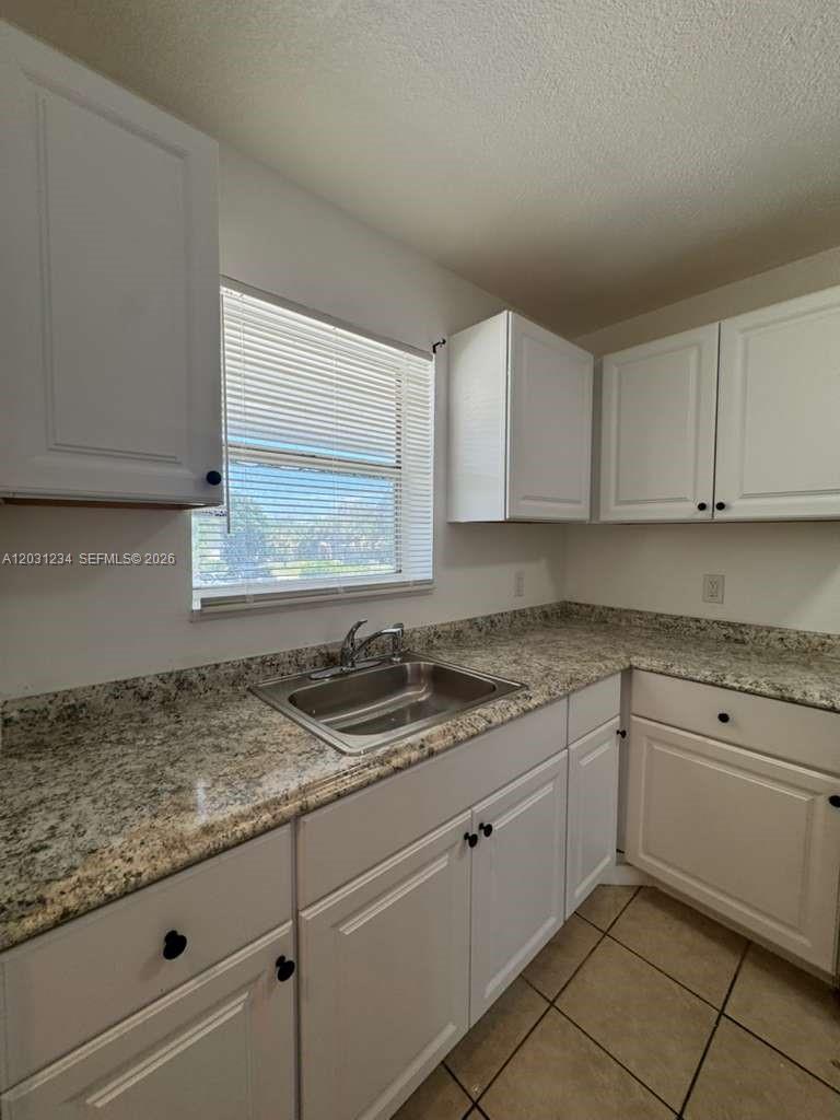 A kitchen features white cabinets, granite countertops, a stainless steel sink, and tile flooring — RIVIERA BEACH, FL