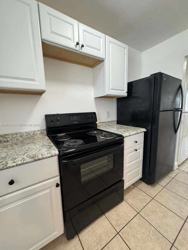 A kitchen features white cabinets, black appliances, and speckled countertops over tiled flooring — RIVIERA BEACH, FL
