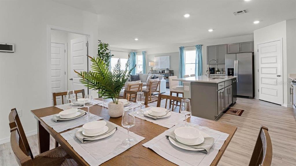 A dining area with a wooden table leads into an open-concept kitchen and living room — 7881 FORREST FOX WAY, LAKELAND, FL