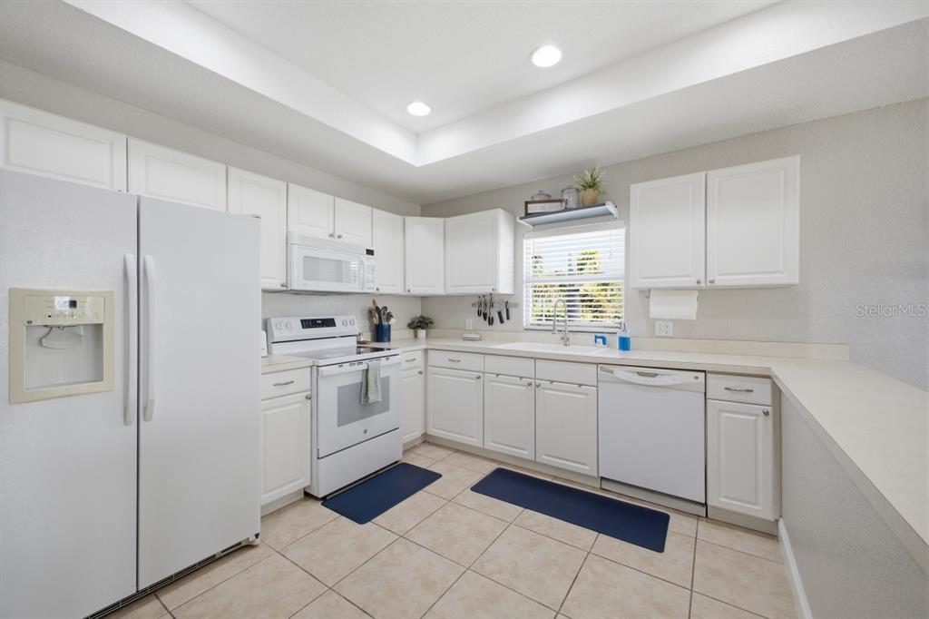 A kitchen features white cabinetry, white appliances, tile flooring, and a window above the sink — 2441 17TH STREET W, PALMETTO, FL