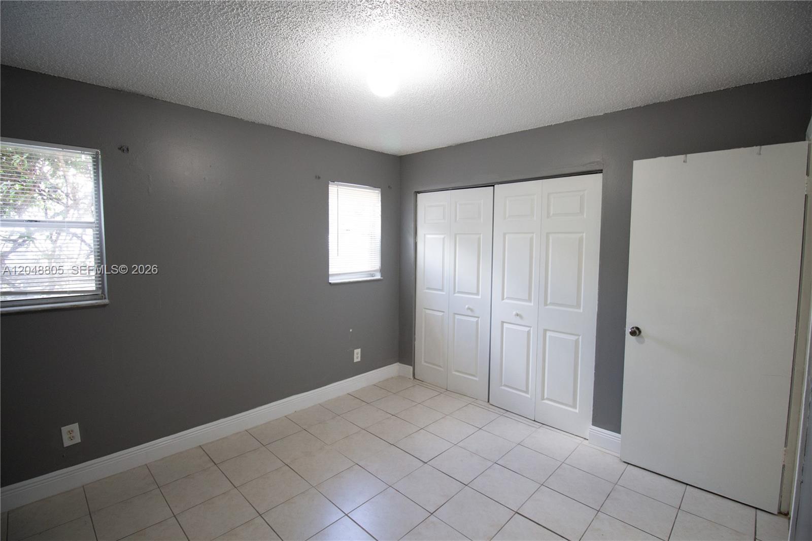 A bedroom with gray walls, white tile flooring, two windows, and white closet doors — 825 SW 10th St # C, Hallandale Beach FL 33009, HALLANDALE BEACH, FL
