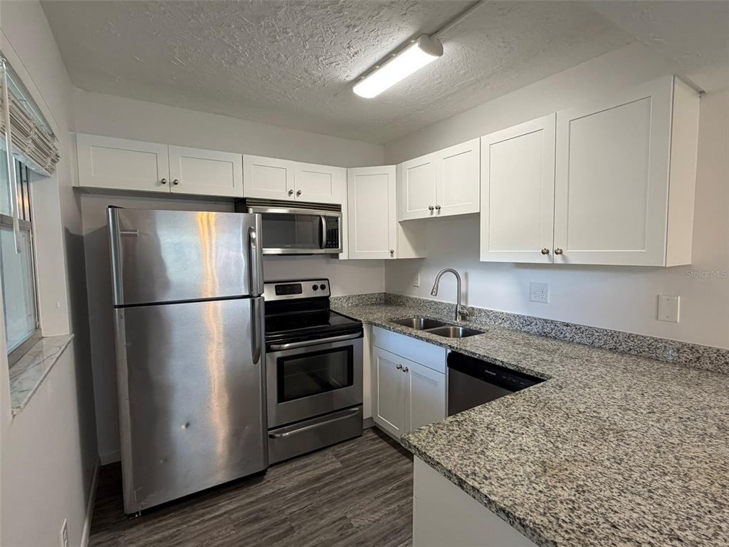 A kitchen features stainless steel appliances, white cabinets, and speckled granite countertops — 7153 W COUNTRY CLUB DR N UNIT 145, SARASOTA, FL