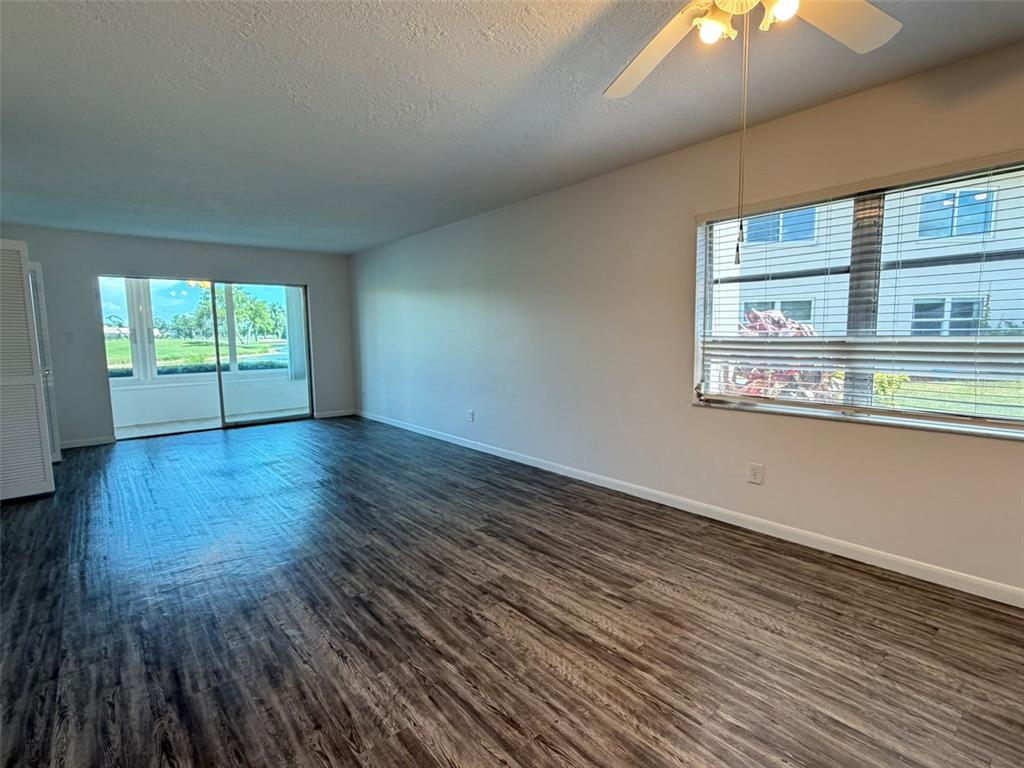 An empty living room features dark wood-look flooring, a ceiling fan, and sliding glass doors — 7153 W COUNTRY CLUB DR N UNIT 145, SARASOTA, FL
