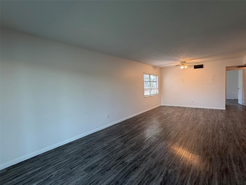 An empty living room features white walls, a ceiling fan, and dark wood-look flooring — 7153 W COUNTRY CLUB DR N UNIT 145, SARASOTA, FL