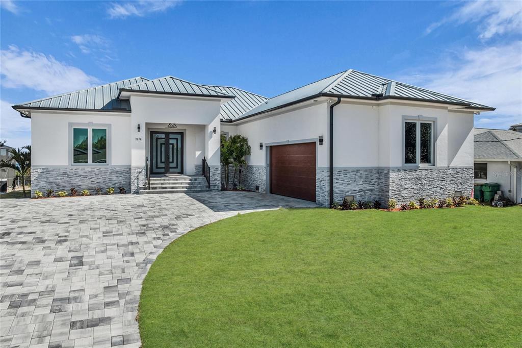 A modern single-story house features a metal roof, white stucco walls, and stone veneer siding — 2228 HARBOUR DRIVE, PUNTA GORDA, FL