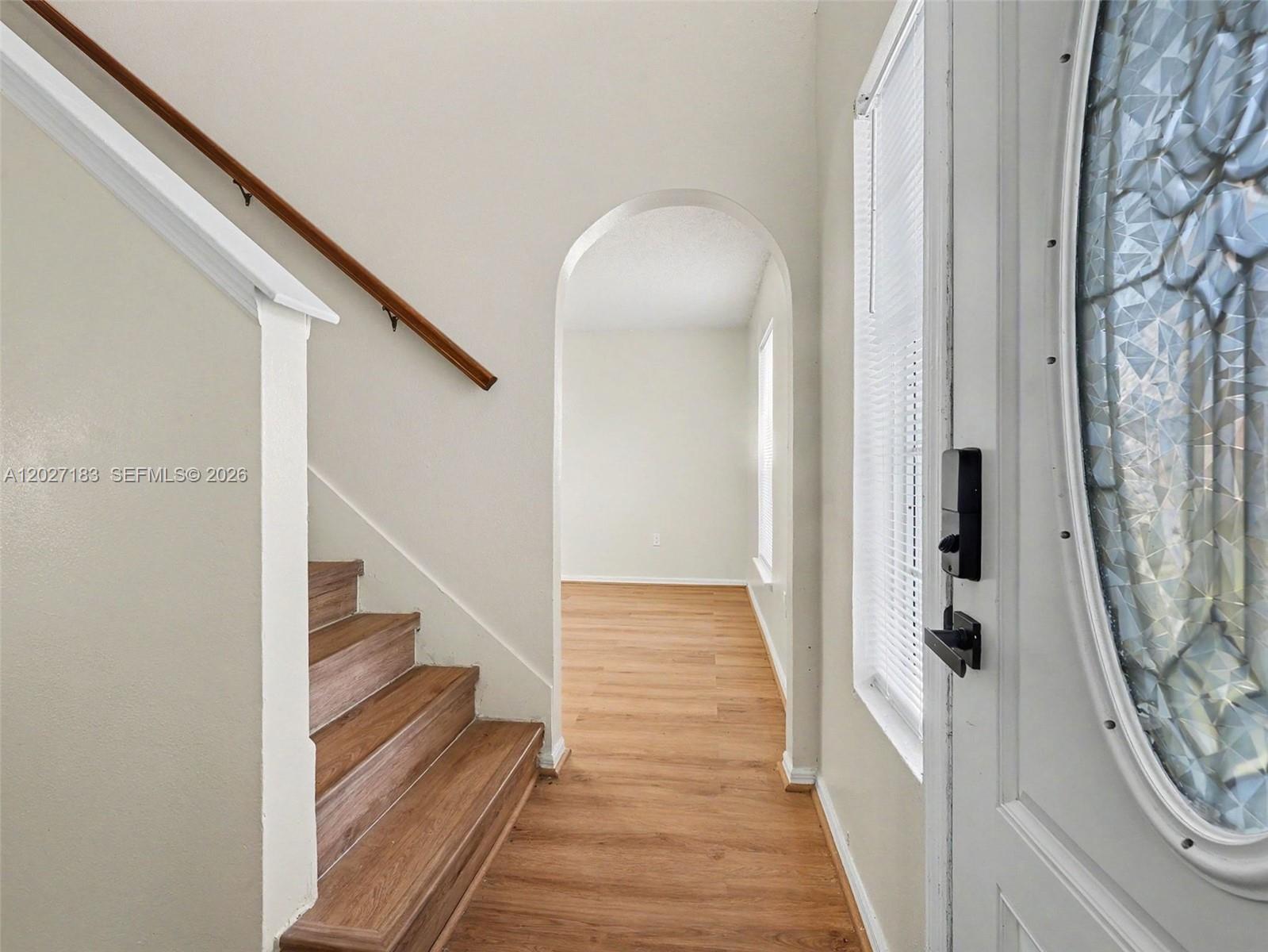 An entryway features a staircase with a wooden handrail, wood-look flooring, and an arched doorway — 945 Gateshead, Kissimmee FL 34758, KISSIMMEE, FL