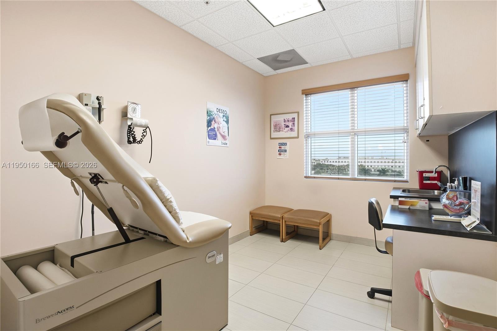 A medical examination room features a beige exam table, two small stools, and a sink — 3650 NW 82nd Ave, Doral FL 33166, DORAL, FL