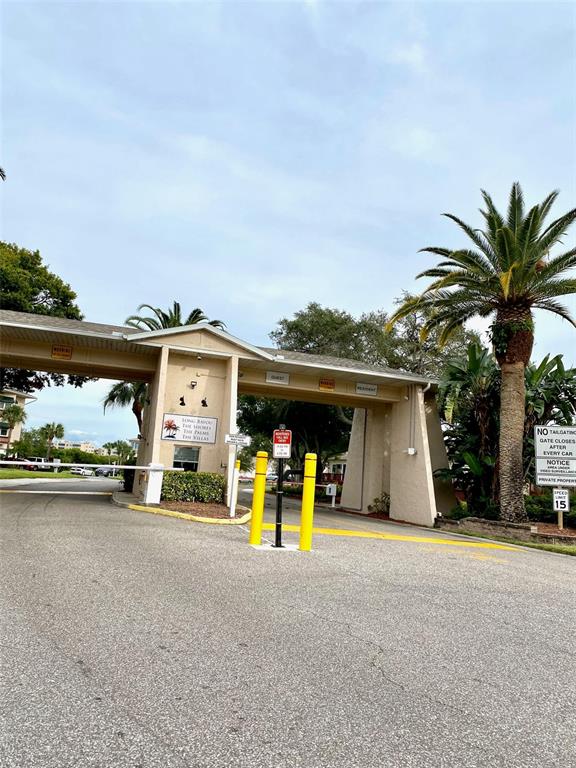 A gated entrance features a beige structure with palm trees and a speed limit sign — 10032 65TH AVENUE N UNIT 17, ST PETERSBURG, FL