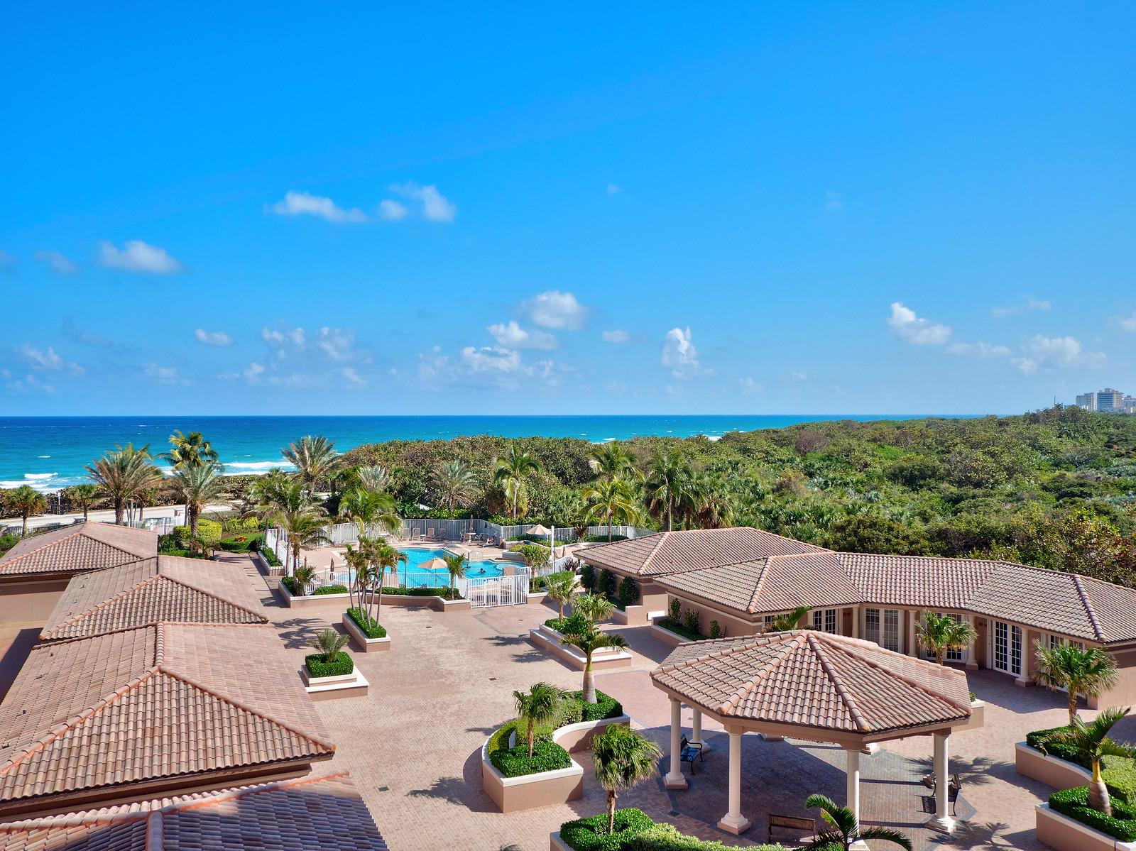 An elevated view of a resort courtyard with a swimming pool, gazebo, and ocean backdrop — 700 Ocean Royale Way # 401, Juno Beach FL 33408, JUNO BEACH, FL