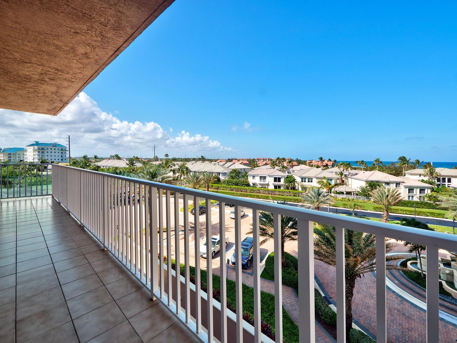 A balcony with white railings overlooks a parking lot, palm trees, and distant coastal homes — 700 Ocean Royale Way # 401, Juno Beach FL 33408, JUNO BEACH, FL