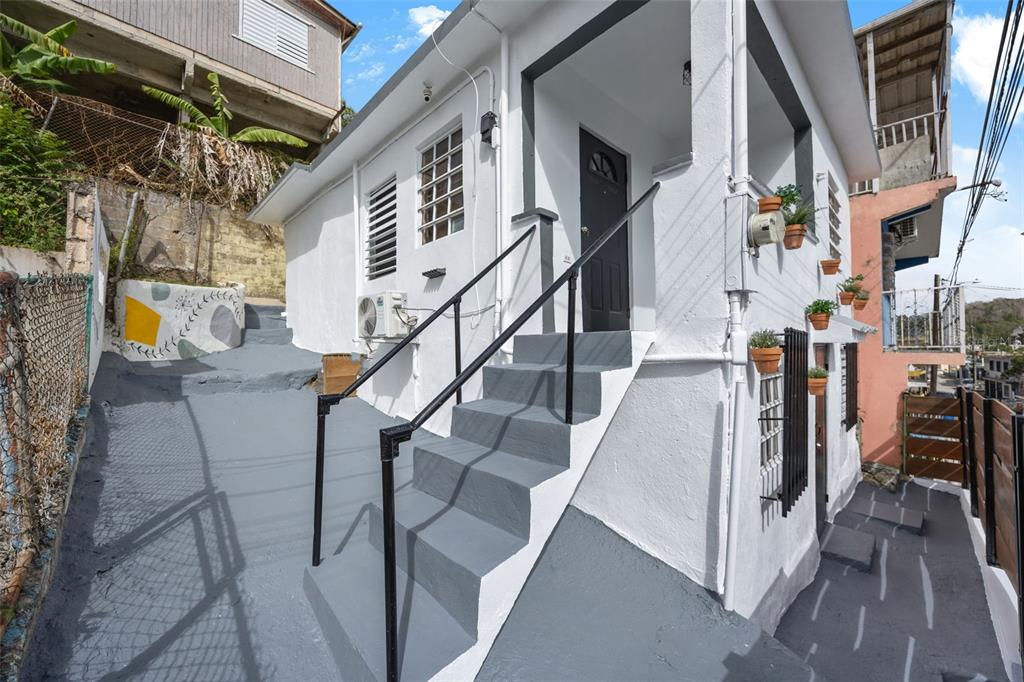 A white house with gray stairs and a painted walkway sits on a sloped lot — JJ-30 CALLE 10, CAYEY, PR