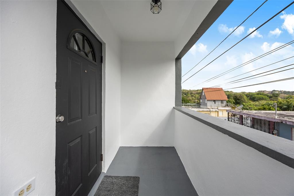 A covered balcony features a black door, gray flooring, and a view of surrounding buildings — JJ-30 CALLE 10, CAYEY, PR