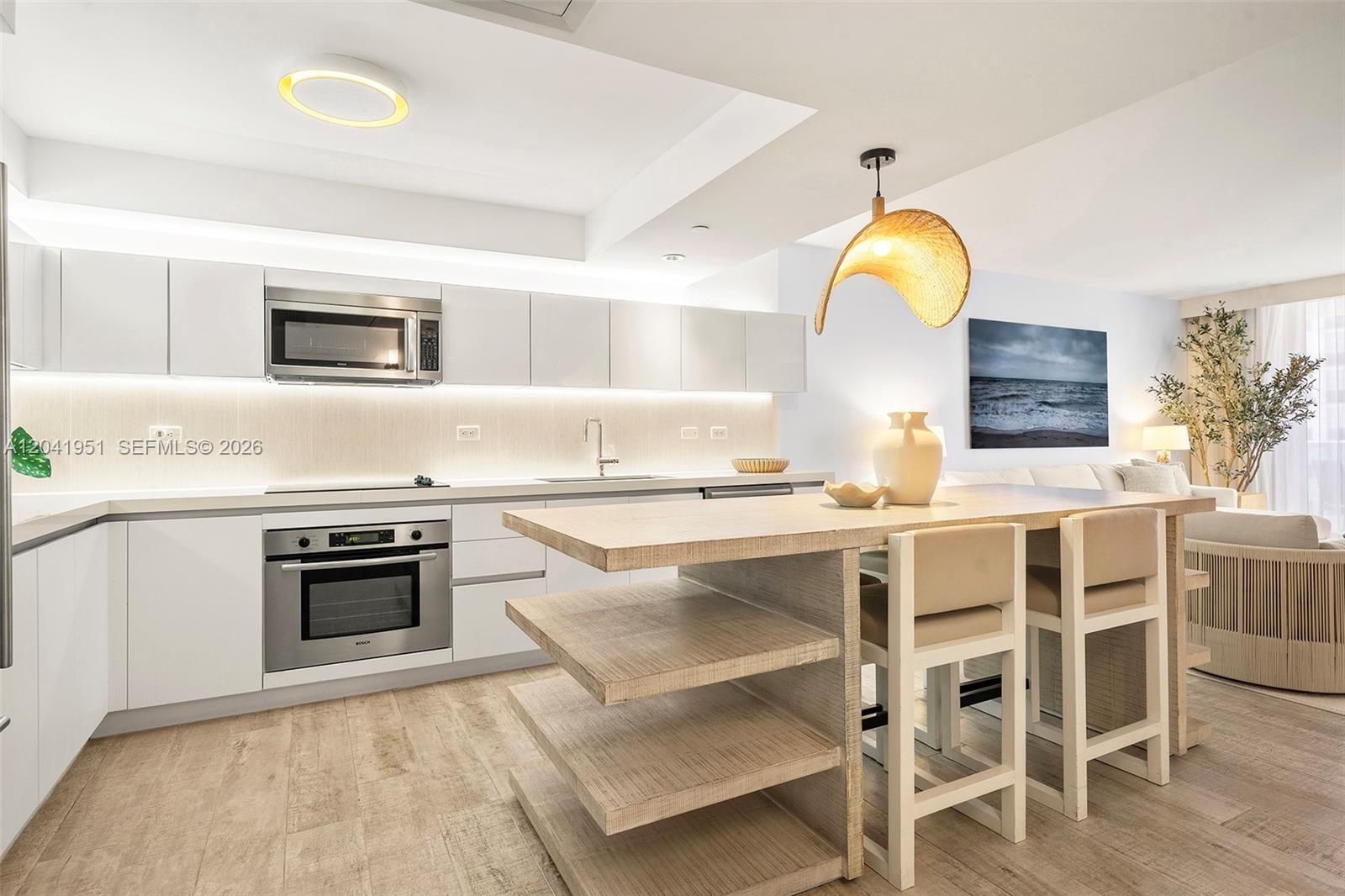 A modern kitchen features white cabinetry, light wood flooring, and a central island with seating — 102 24th St # 1213, Miami Beach FL 33139, MIAMI BEACH, FL