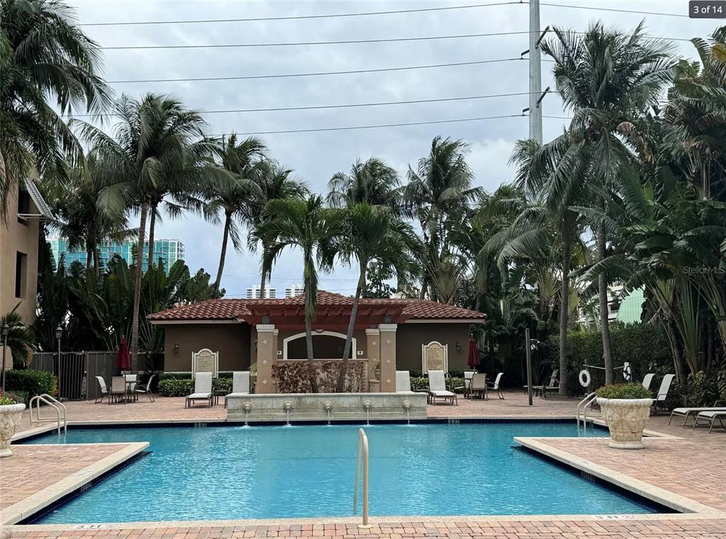 A swimming pool sits in front of a building with a pergola and palm trees — 616 CLEARWATER PARK ROAD UNIT 1002, WEST PALM BEACH, FL