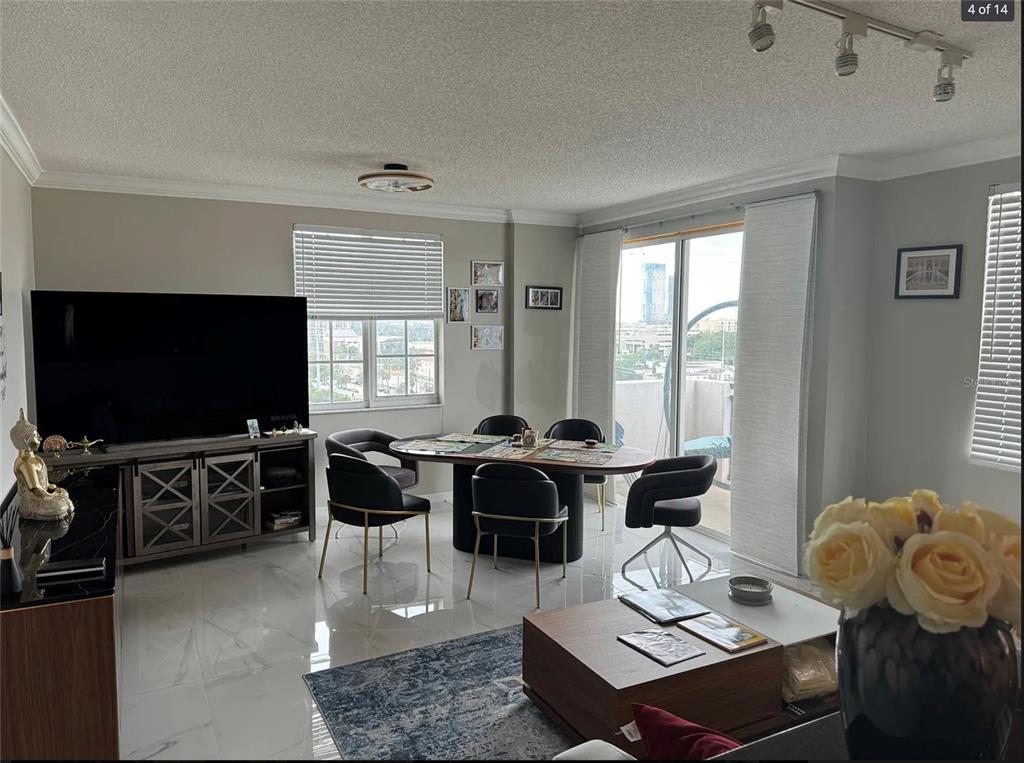 A living and dining area with white tile floors, a television console, and balcony access — 616 CLEARWATER PARK ROAD UNIT 1002, WEST PALM BEACH, FL