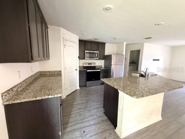 A kitchen features dark wood cabinets, granite countertops, stainless steel appliances, and light wood flooring — 3494 APPLE ORCHARD DRIVE, DELTONA, FL