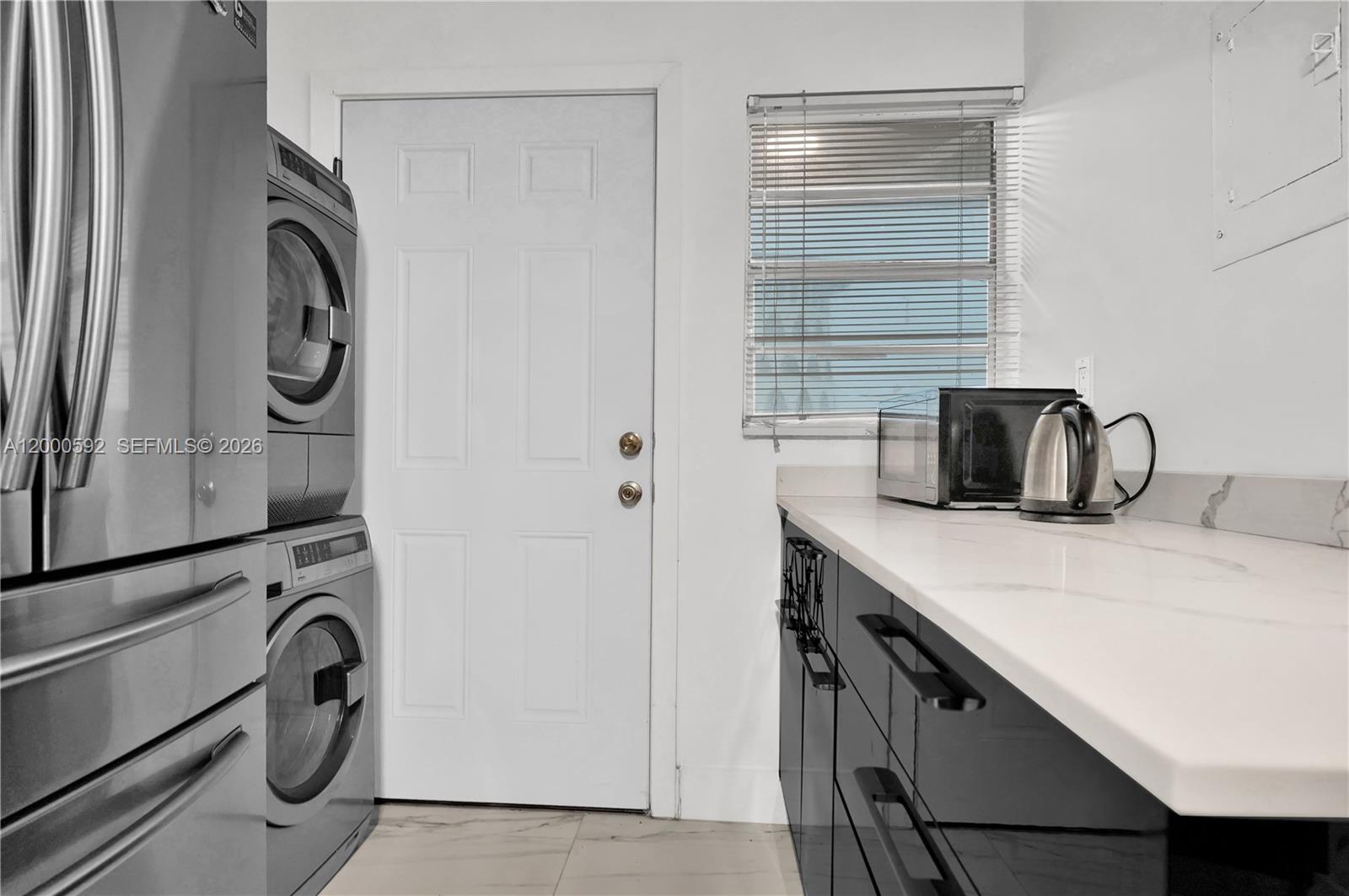 A laundry area features a stacked washer and dryer, white door, and black cabinets — 1750 NE 191st St # 2, Miami FL 33179, MIAMI, FL