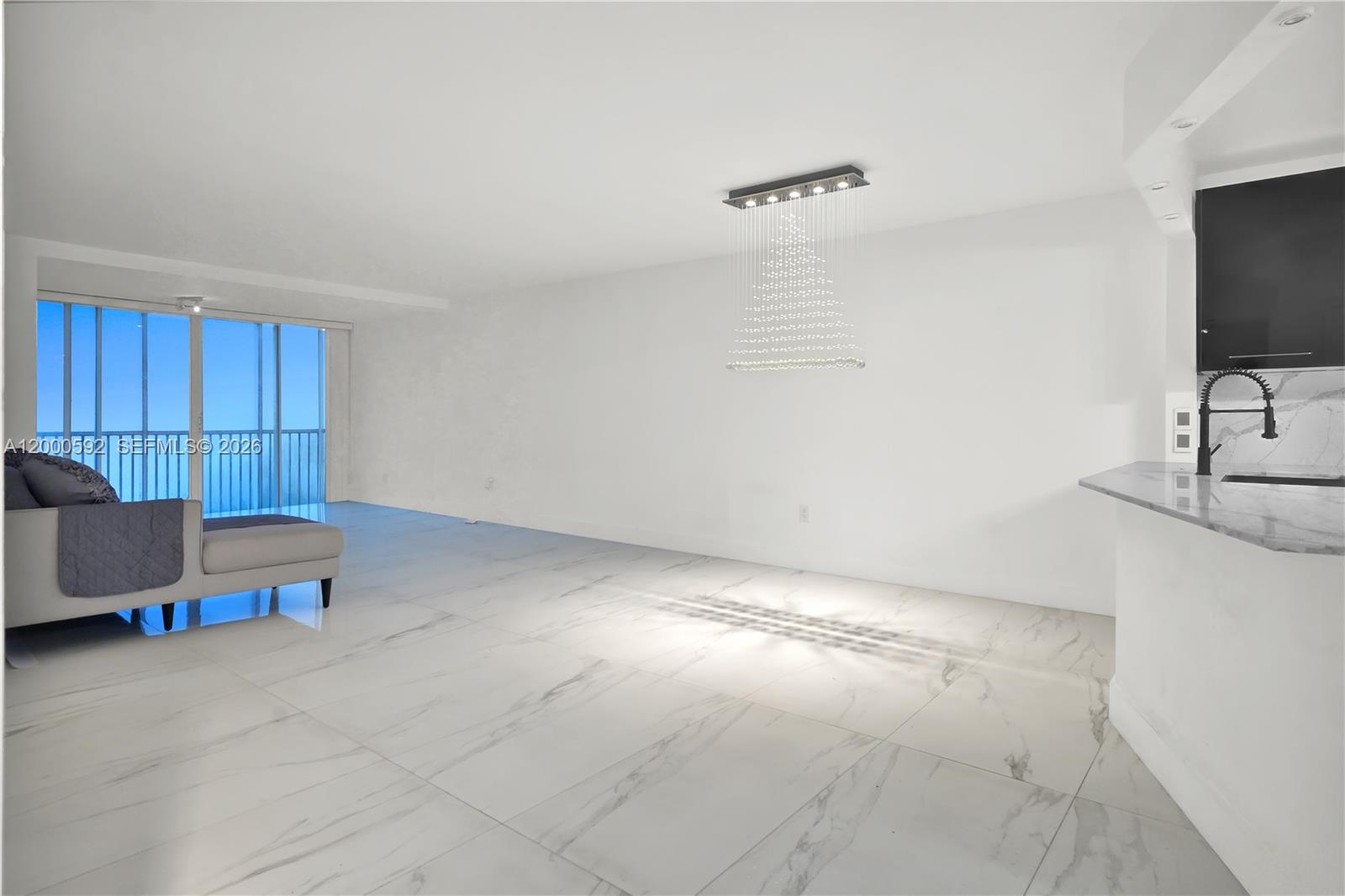 A living room with white marble floors, a modern crystal chandelier, and a balcony view — 1750 NE 191st St # 2, Miami FL 33179, MIAMI, FL