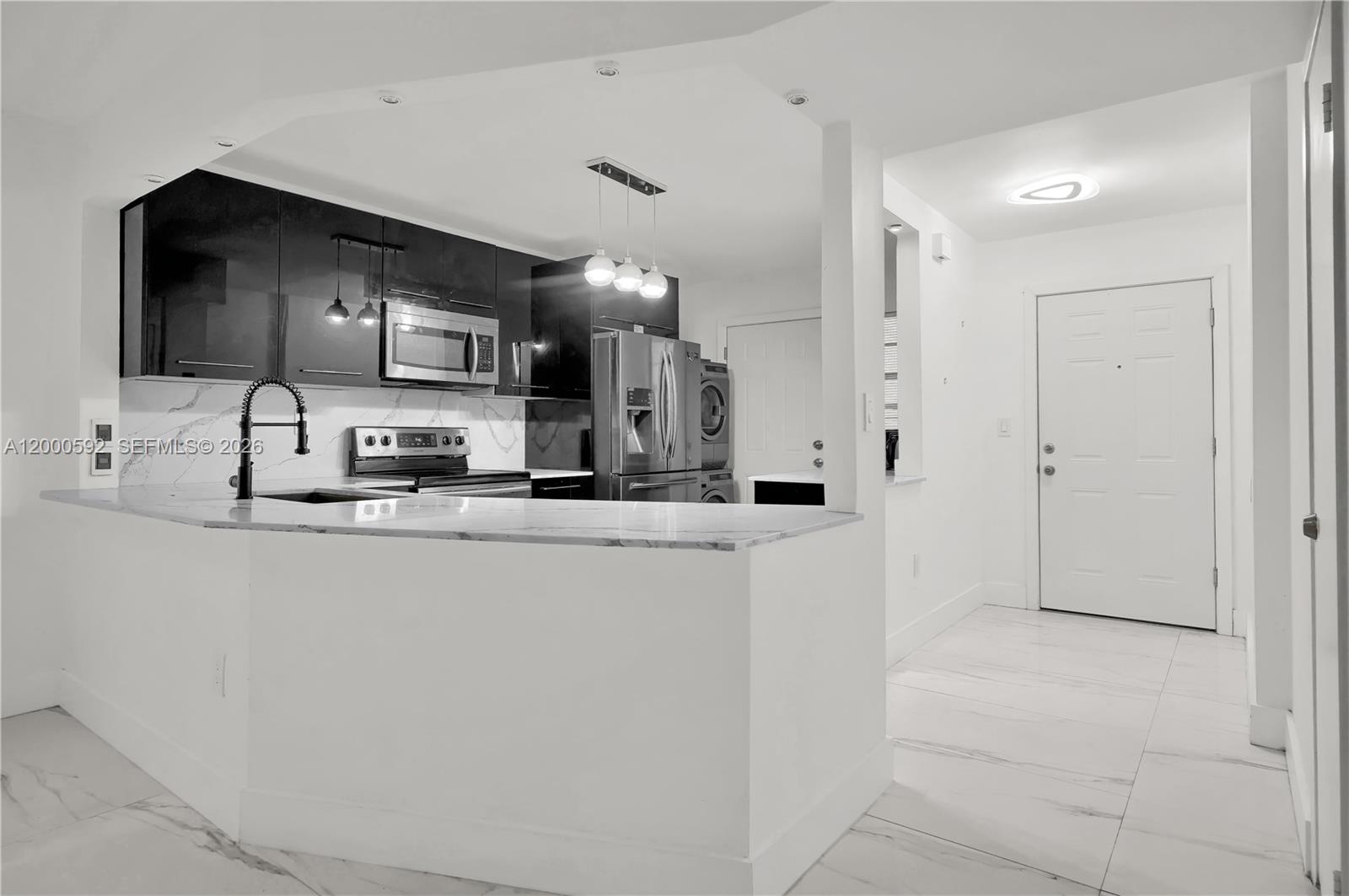 A modern kitchen features dark cabinetry, stainless steel appliances, and a white marble-topped breakfast bar — 1750 NE 191st St # 2, Miami FL 33179, MIAMI, FL