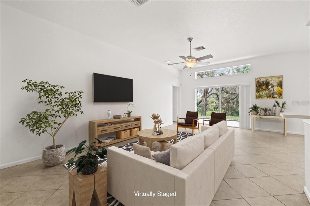 A living room with tile floors, a sofa, a television, and a view of trees — 13102 EARLY RUN LANE, RIVERVIEW, FL
