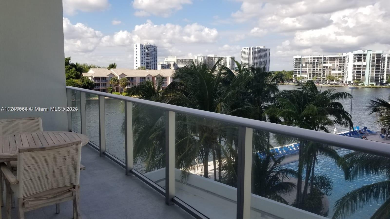 A balcony overlooks a swimming pool, palm trees, a lake, and distant apartment buildings — 4010 S Ocean Dr # R301, Hollywood FL 33019, HOLLYWOOD, FL
