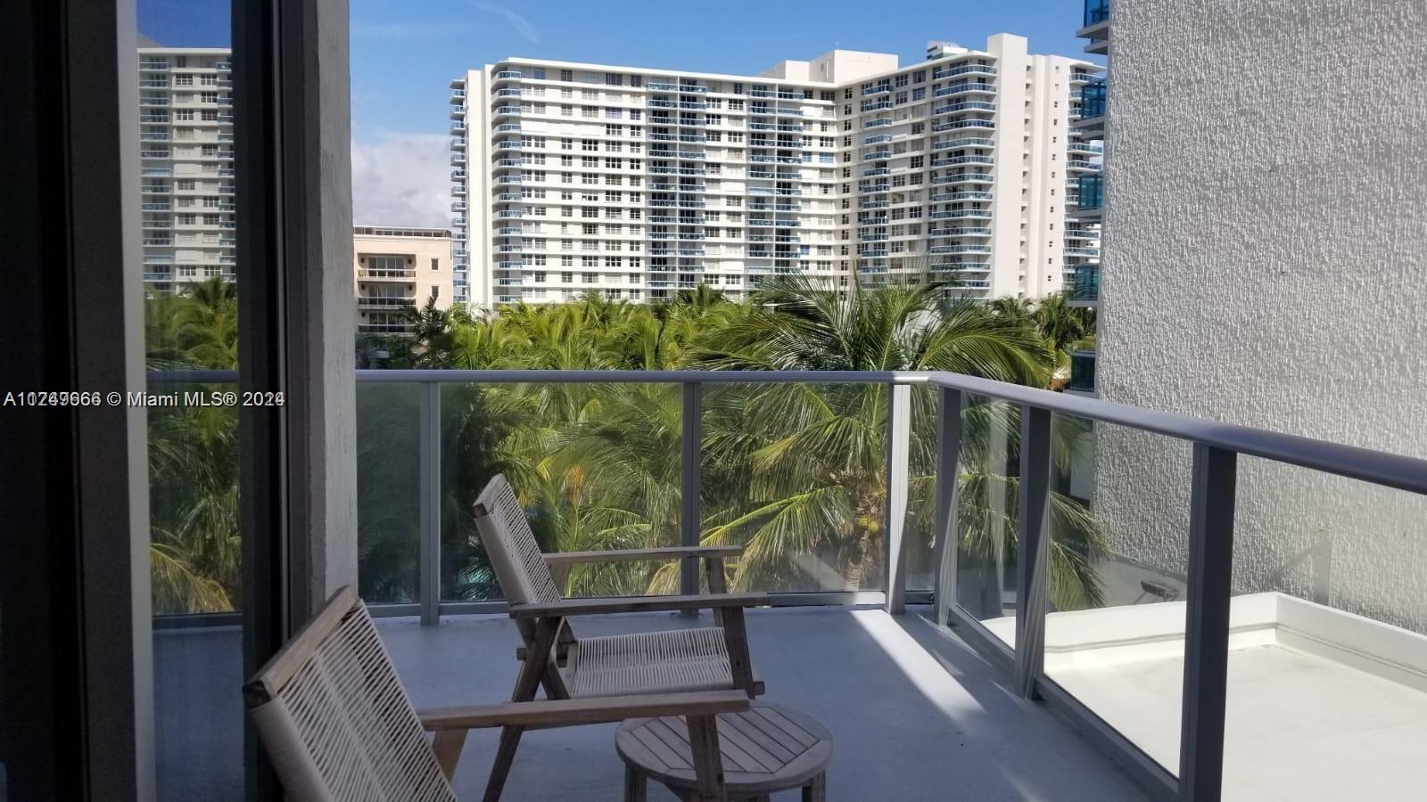 A balcony with two wooden chairs and a small table overlooks palm trees and buildings — 4010 S Ocean Dr # R301, Hollywood FL 33019, HOLLYWOOD, FL
