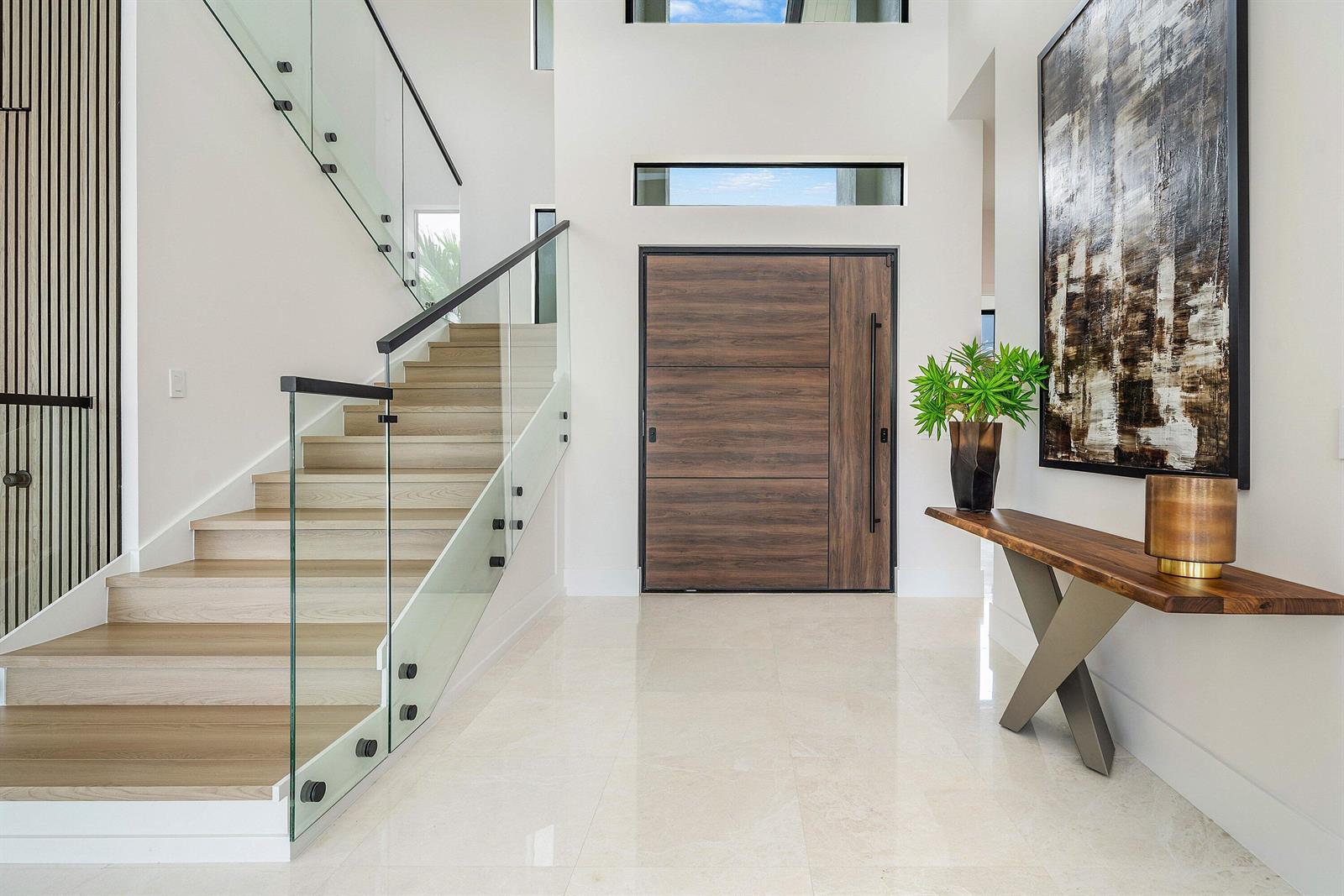 A modern foyer features a wood-paneled door, glass-railed staircase, and a live-edge console table — 798 Havana Drive, Boca Raton FL 33487, BOCA RATON, FL