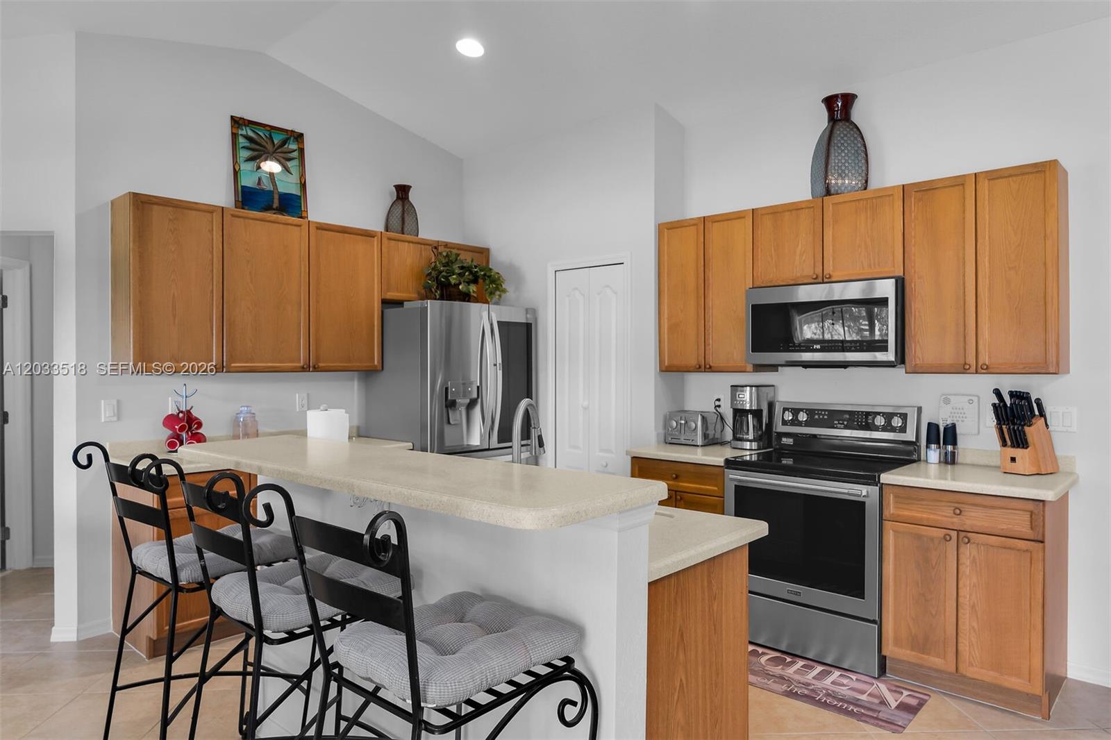 A kitchen features wood cabinets, stainless steel appliances, and a breakfast bar with three chairs — 2009 SW 36th Ter, Cape Coral FL 33914, CAPE CORAL, FL