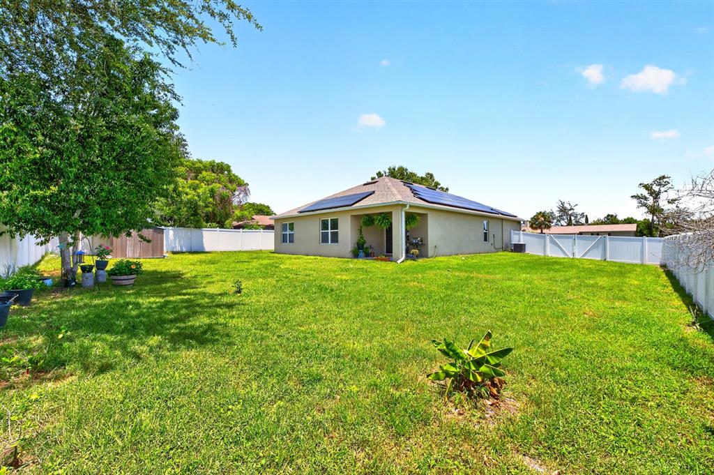 A backyard with a green lawn, a house with solar panels, and a white fence — 1191 ABAGAIL DRIVE, DELTONA, FL