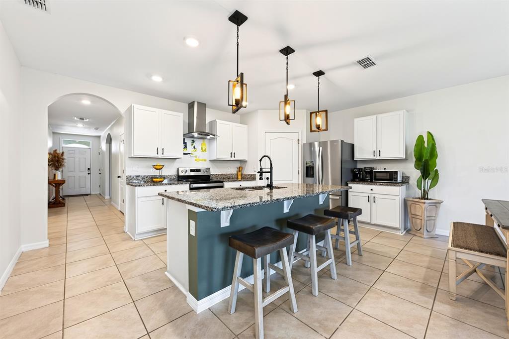 A kitchen features white cabinets, granite countertops, a dark green island, and three pendant lights — 1191 ABAGAIL DRIVE, DELTONA, FL