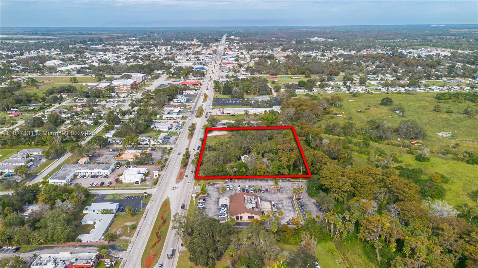 An aerial view shows a rectangular, tree-covered vacant lot outlined in red next to a commercial building — 1011 S. PARROTT, Okeechobee FL 34972, OKEECHOBEE, FL