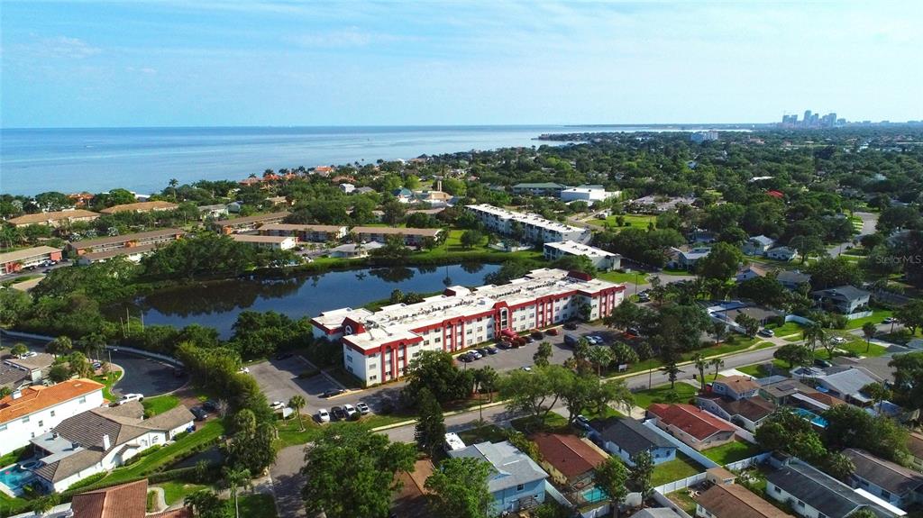 An aerial view shows a multi-story apartment complex situated near a lake and coastline — 1860 MASSACHUSETTS AVENUE NE UNIT 224, ST PETERSBURG, FL