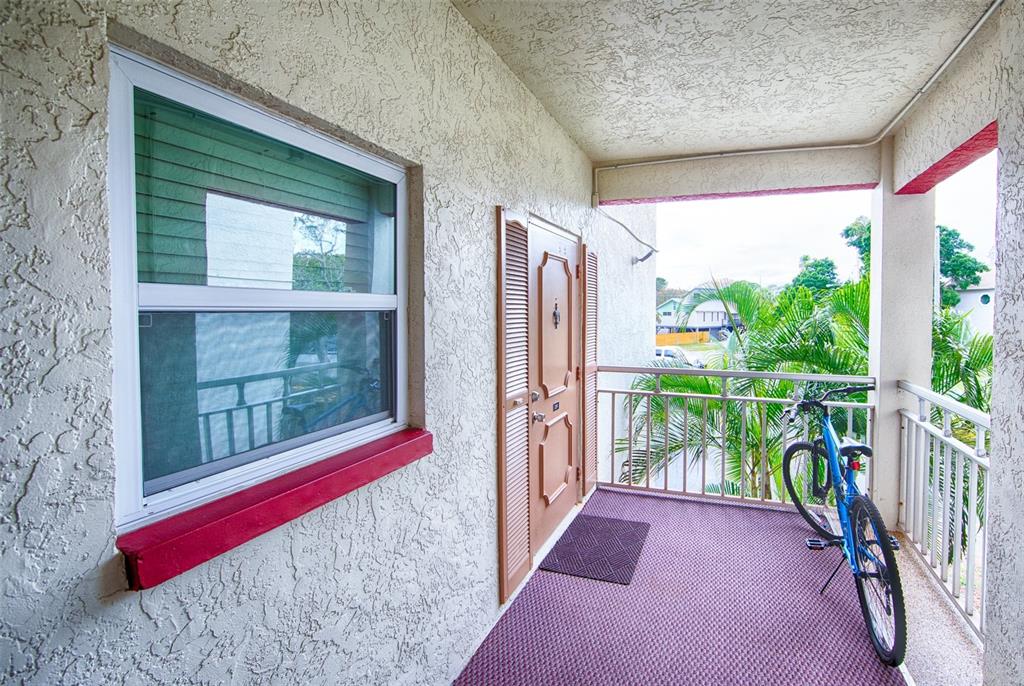 A covered balcony features a textured wall, a window with a red sill, and a bicycle — 1860 MASSACHUSETTS AVENUE NE UNIT 224, ST PETERSBURG, FL