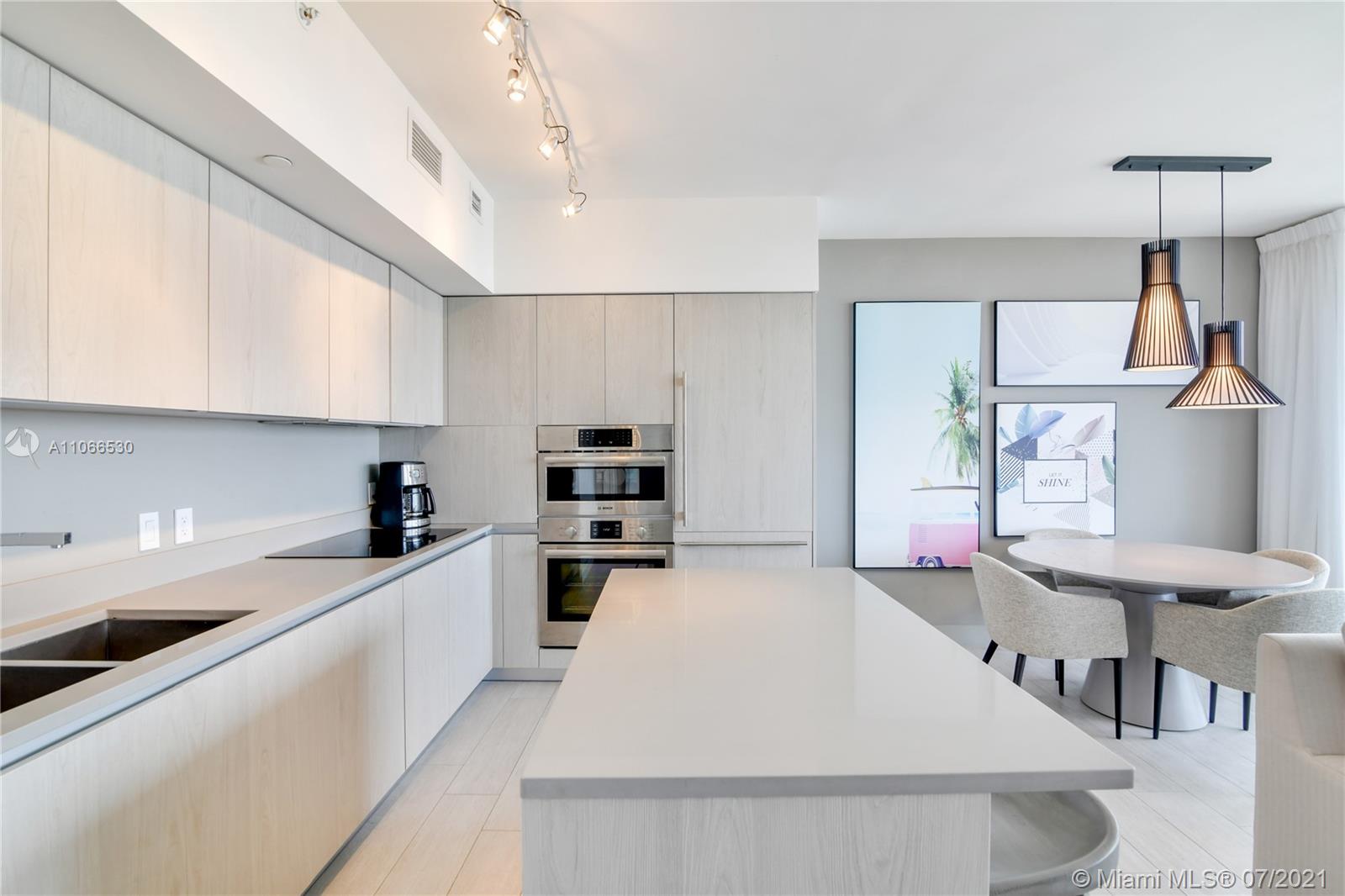 A modern kitchen features light wood cabinetry, a central island, and an adjacent dining area — 4010 S Ocean Dr # R1406, Hollywood FL 33019, HOLLYWOOD, FL