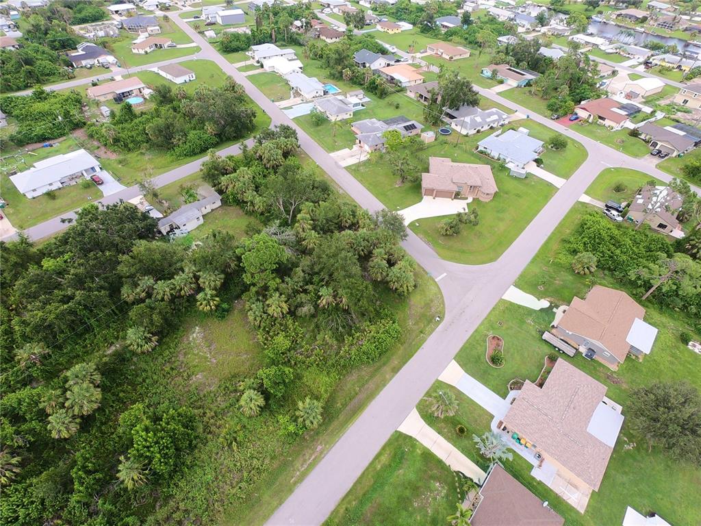 An aerial view shows a suburban neighborhood with houses, paved streets, and wooded lots — 506 FAIRVIEW AVENUE NW, PORT CHARLOTTE, FL