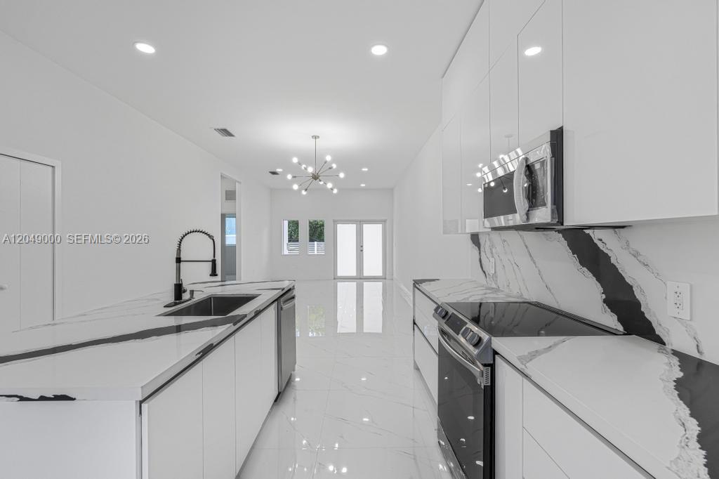 A modern kitchen features white cabinets, black and white marble countertops, and tile flooring — 2419 NW 97th St, Miami FL 33147, MIAMI, FL