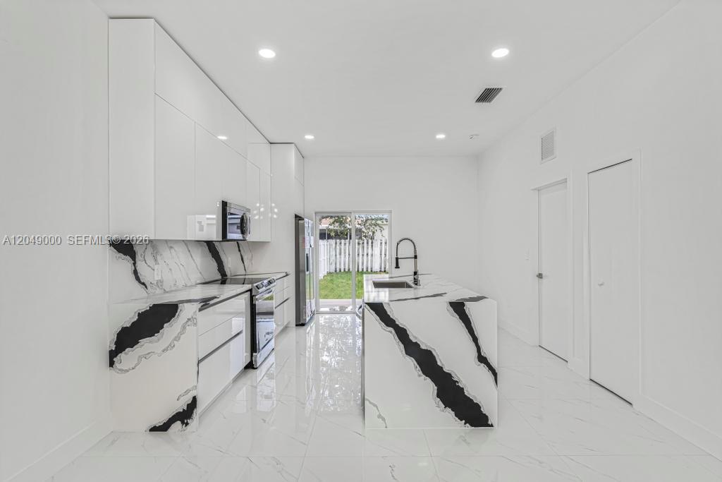 A modern kitchen features white glossy cabinets, black and white marble countertops, and tile flooring — 2419 NW 97th St, Miami FL 33147, MIAMI, FL