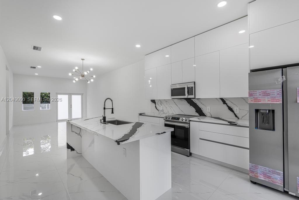A modern kitchen features white glossy cabinets, a marble-patterned island, and stainless steel appliances — 2419 NW 97th St, Miami FL 33147, MIAMI, FL