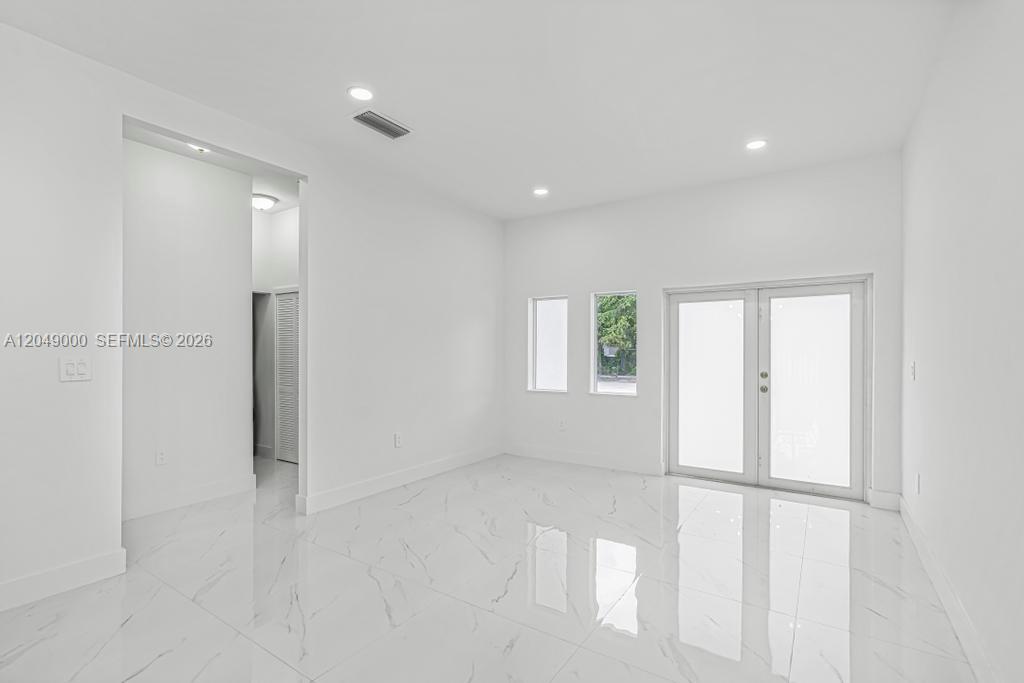 A bright, empty room features white walls, recessed lighting, and polished white marble-look tile flooring — 2419 NW 97th St, Miami FL 33147, MIAMI, FL