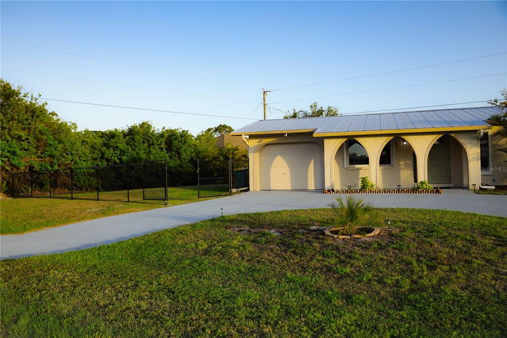 A single-story house with a metal roof, arched porch, and attached garage sits on a lawn — 389 MILLPORT STREET NW, PORT CHARLOTTE, FL